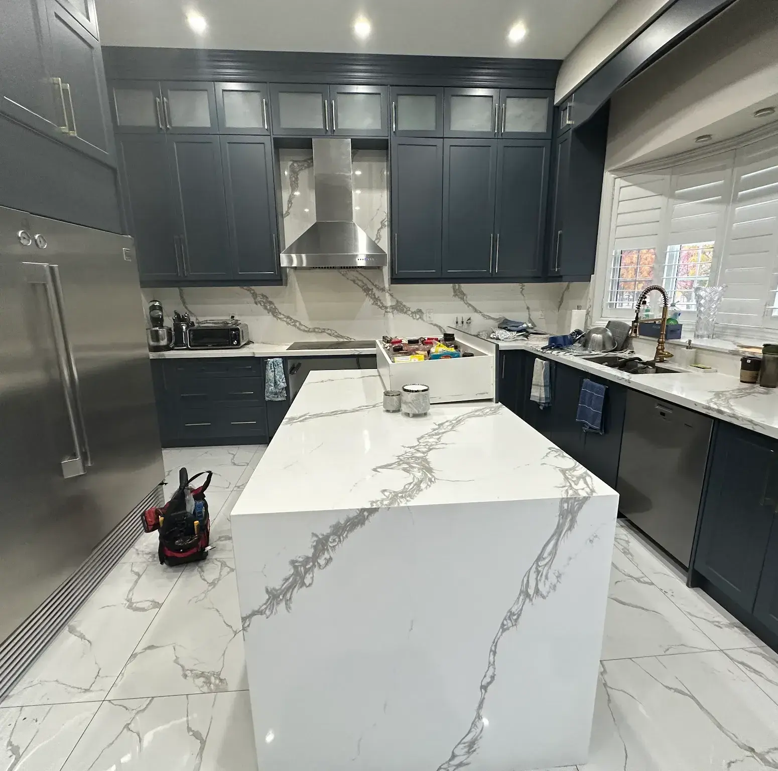 Navy shaker kitchen with a waterfall quartz island, mid-install