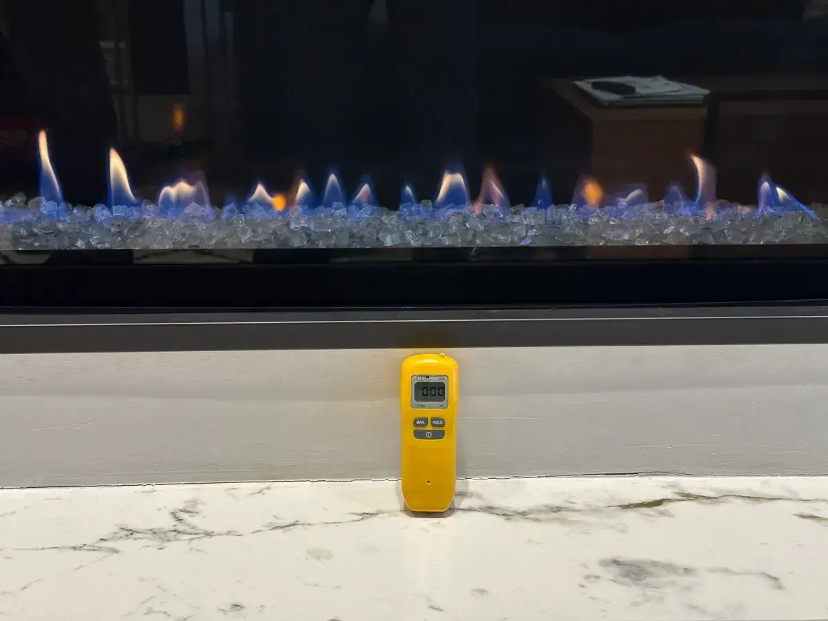 Handheld carbon monoxide meter reading 000 ppm in front of a lit gas appliance