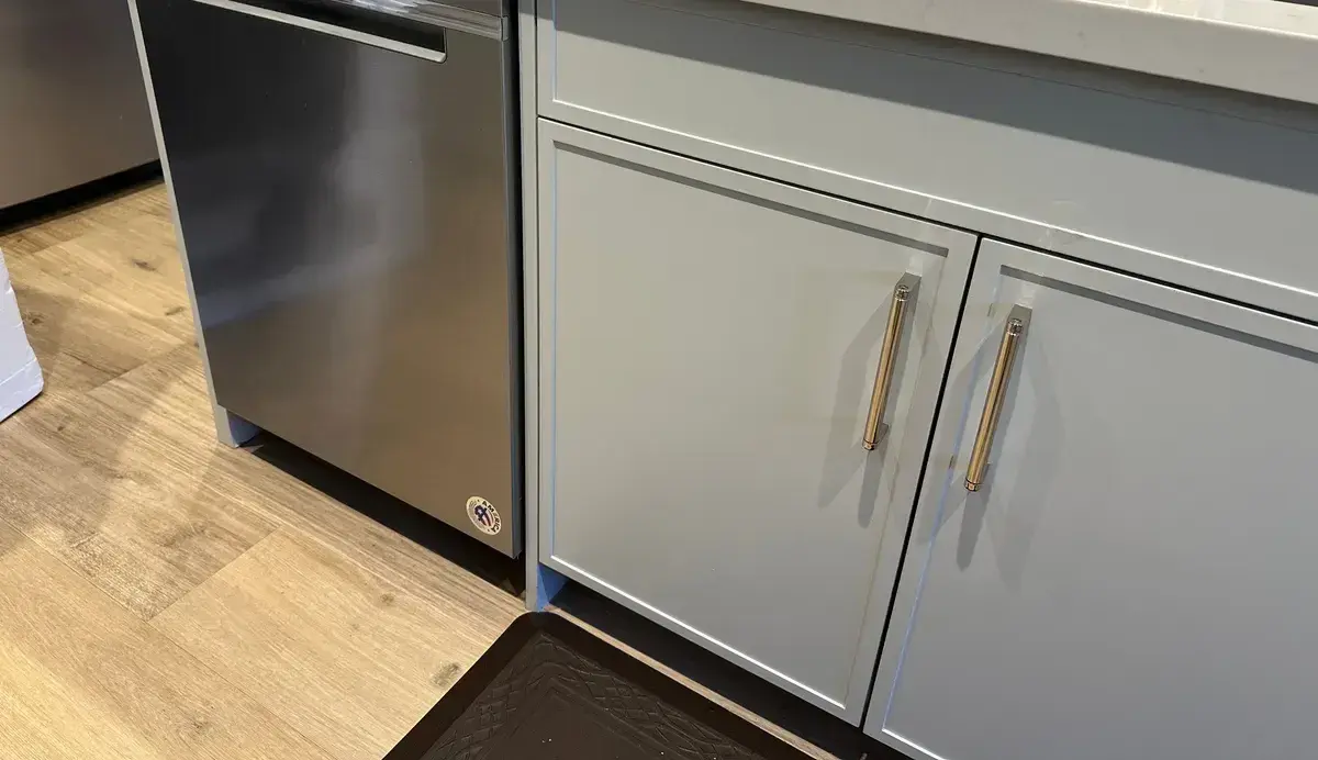 Stainless dishwasher installed in a grey and white kitchen with quartz counters and brass hardware