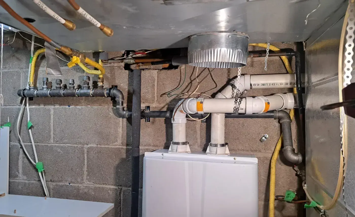 Basement mechanical room with a black-iron gas manifold, six valved take-offs, labelled copper drops for BBQ and gas dryer, and a tankless water heater with twin PVC vents