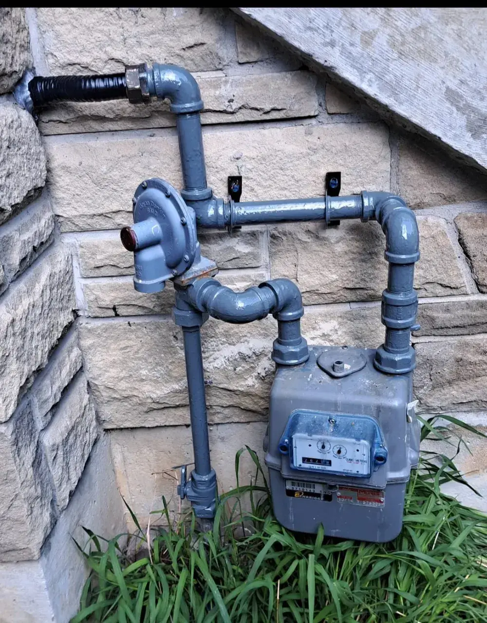 The same gas meter re-piped with new painted steel pipe and a sealed wall entry