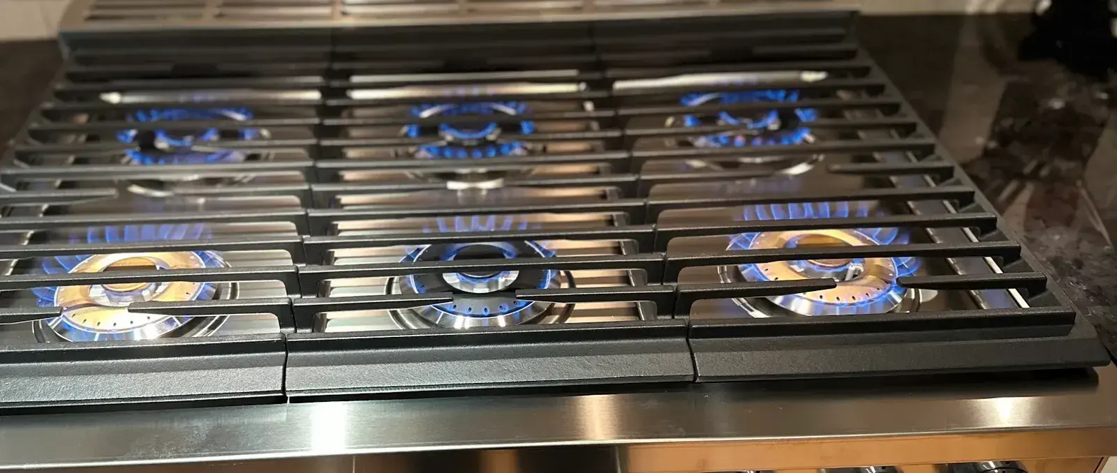 Gas cooktop burners lit blue across a stainless range during the final flame test