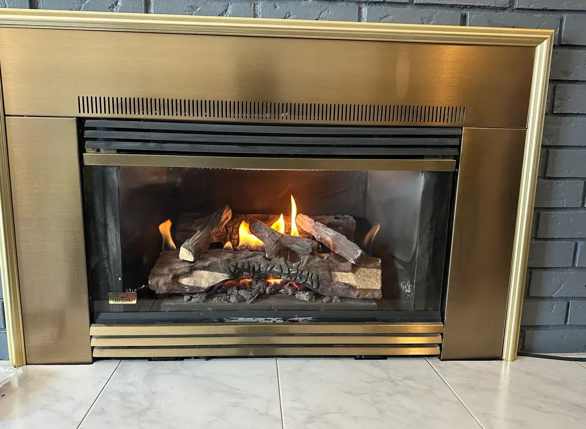 Napoleon gas fireplace insert with brass surround burning in a grey-painted brick chimney breast