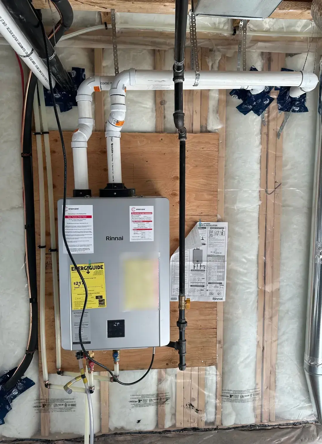 Rinnai tankless water heater installed with twin PVC vent runs and a black iron gas line