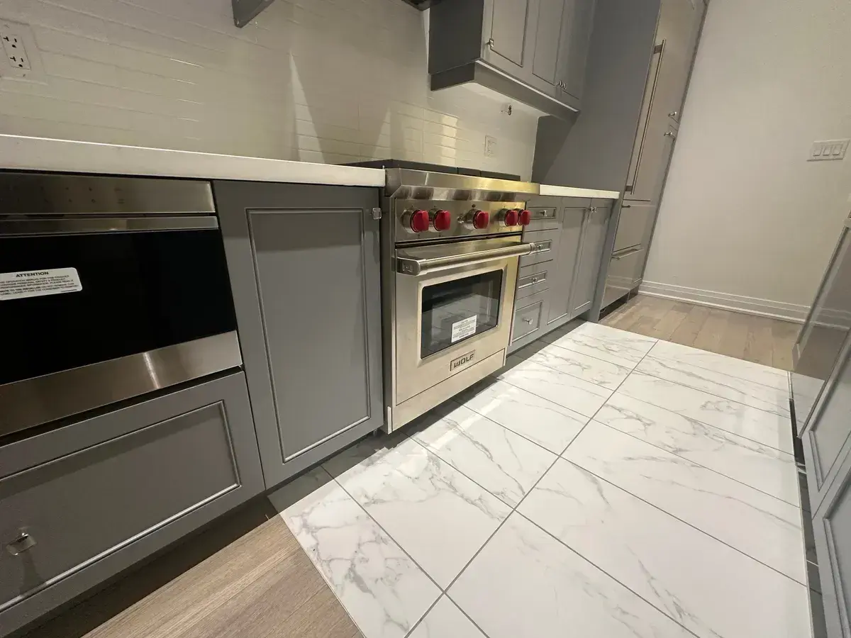 Wolf gas range with red knobs in a grey shaker kitchen with marble floor
